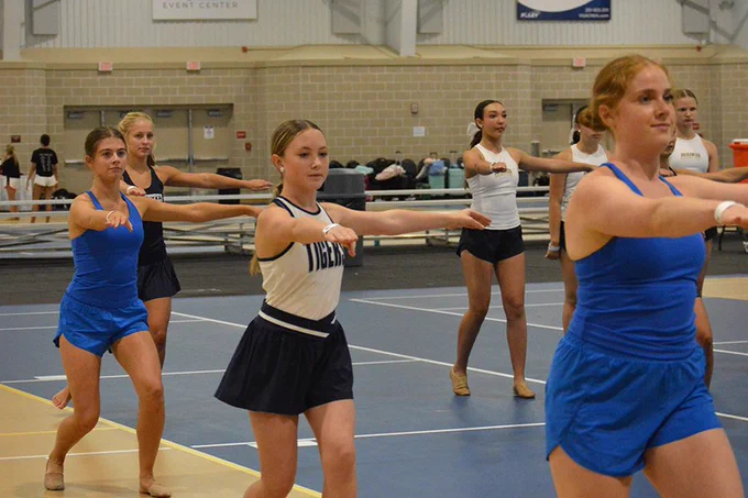 A group of dancers with one foot in front of the other and knees bent preparing for a turn with one arm out in front and one to the side.