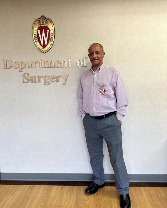 Dr. Nebyou Seyoum Abebe stands in front of a sign that says "Department of Surgery" with the UW crest