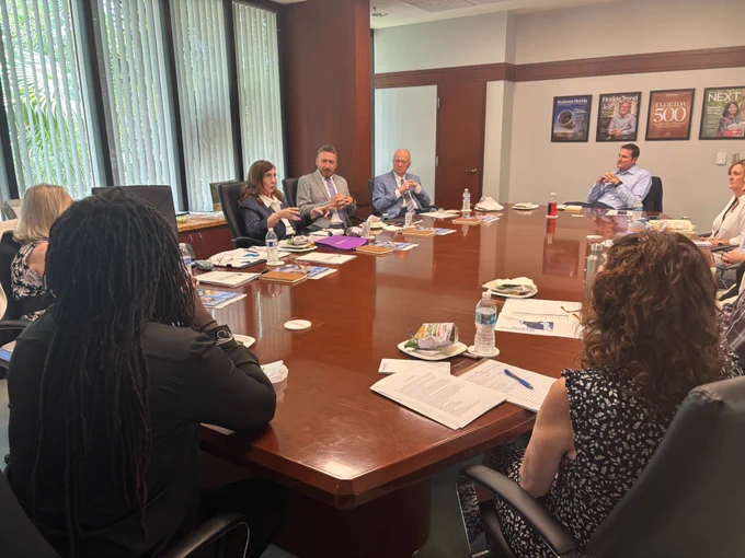 Drs. Judith Bilsky and Jeffery Allbritten, accompanied by Jason Dudley, speak with members of the Florida Trend Editorial Board in a large, well-lit boardroom. 