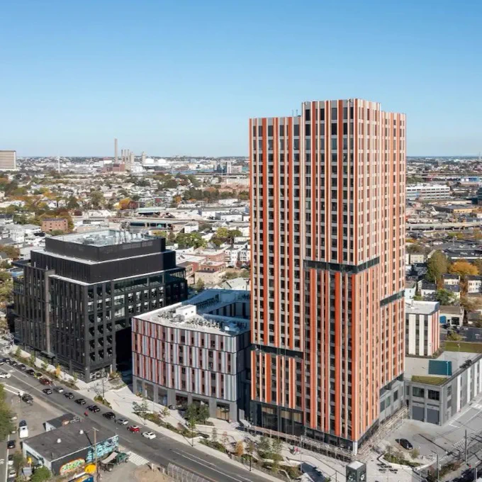 Aerial view of the Somerville, Massachusetts area with three brand new buildings, one with black siding, the middle has a gray exterior, and the tallest building has a orange exterior. 