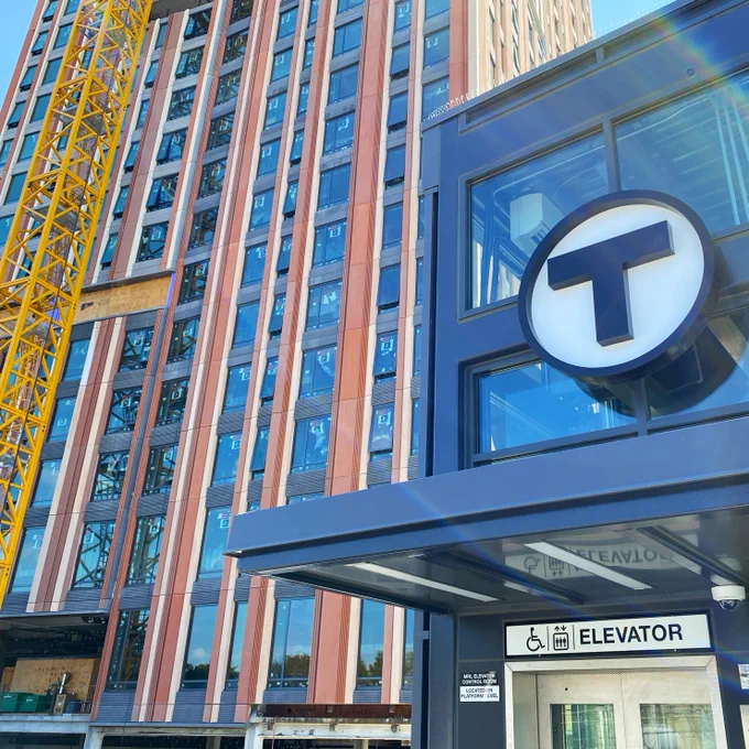 Close up of an MBTA stop in front of a new construction building, with a yellow crane body to the left of the photo.