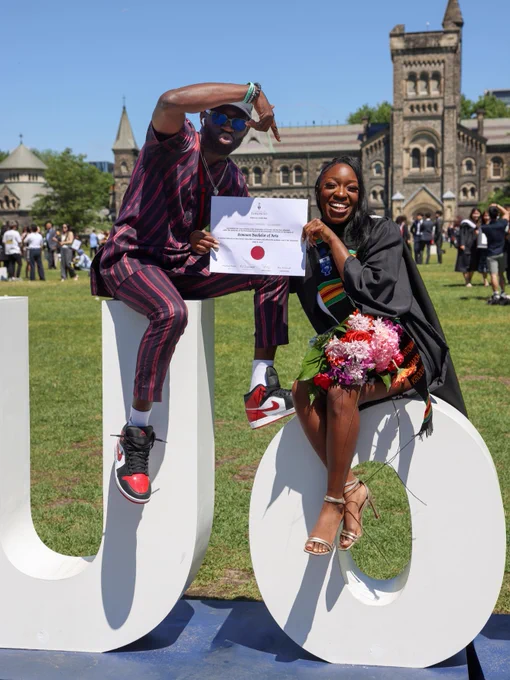 UTSC graduates poses excitedly with the certificate, seated on top of the large white letters "U of T".