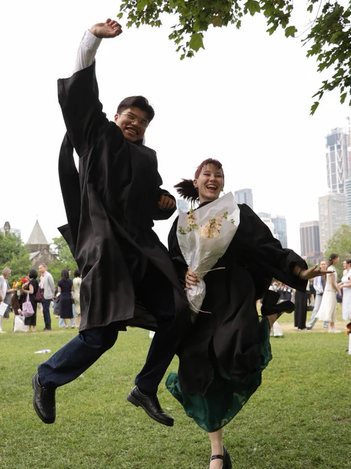 UTSC graduates joyfully jumping in the air on a grassy area.