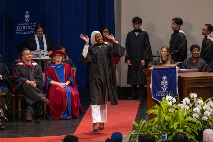 UTSC graduate waving joyfully while walking across a stage at a U of T Scarborough graduation ceremony. 