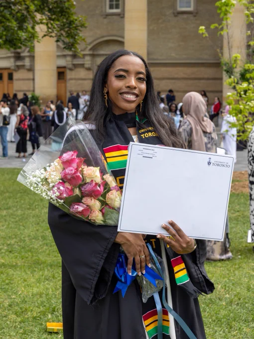 UTSC graduate wearing a graduation gown and coluorful stole holds a bouquet of pink and white flowers as well as the certificate.