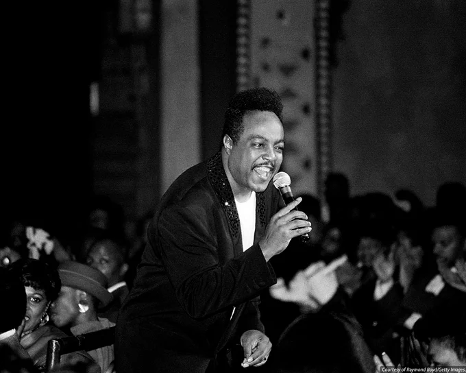 Black-and-white photo of Peabo Bryson performing with a microphone. At the bottom is a credit line reading, 'Courtesy of Raymond Boyd/Getty Images.'
