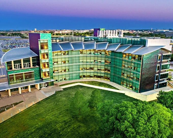 A drone photo of NSERL at dusk, with a purple and blue sky above and lush greenery in front of the building
