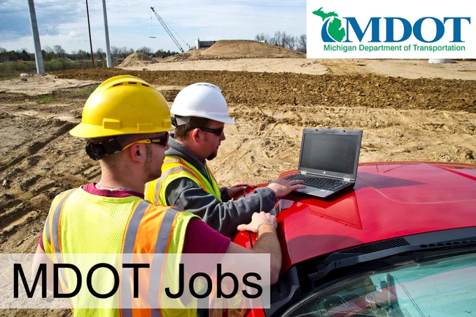 Two workers in safety gear look at a laptop at a jobsite.