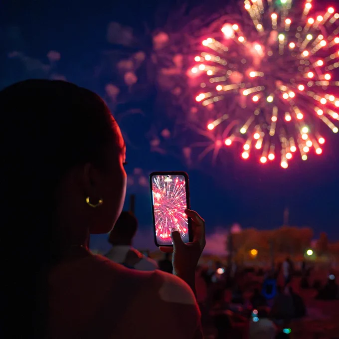 Person holding phone filming fireworks at night
