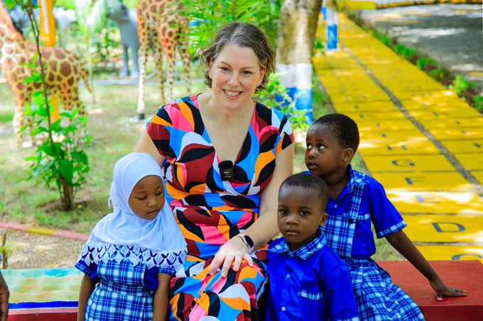 MSU Associate Professor Bethany Wilinski smiles with children in Tanzania at a playscape. 