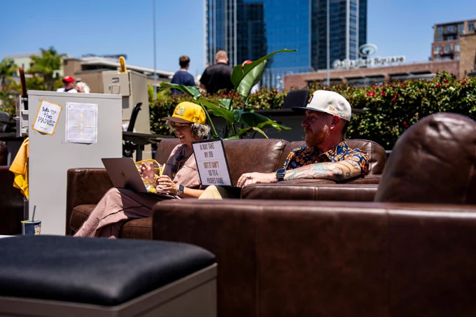 Photo of two Padres fans sitting on a couch in Gallagher Square. They are both working on their laptops for Remote Work Wednesdays.