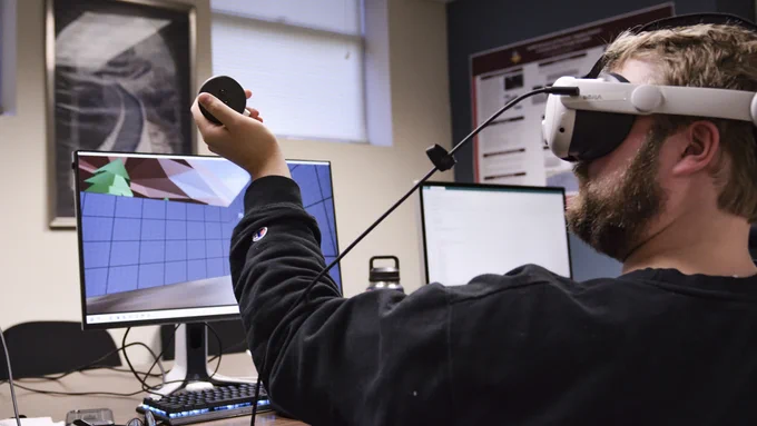 Student wearing a virutal reality headset, computer in background