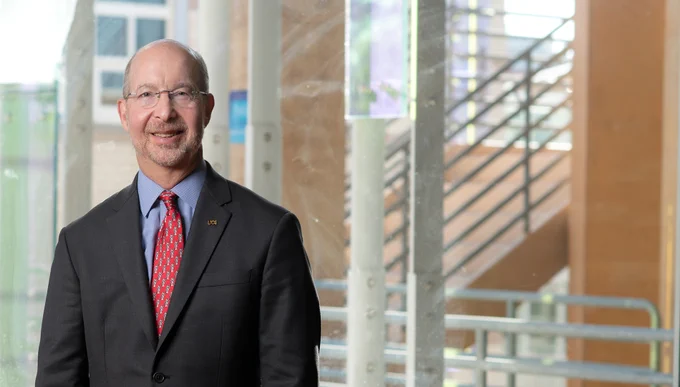 Jon B. Gould, dean of the UC Irvine School of Social Ecology, is shown indoors near large windows with a modern staircase in the background. Photo by Steve Zylius / UC Irvine