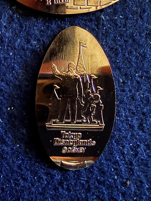 Souvenir medal ("pressed penny") of the view of the Tokyo Disneyland Partners Stature. Text: "Tokyo Disneyland" ©Disney

