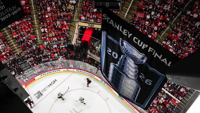 A large banner displaying 'Stanley Cup Final 2026' hangs over a packed hockey arena filled with fans in red seats.