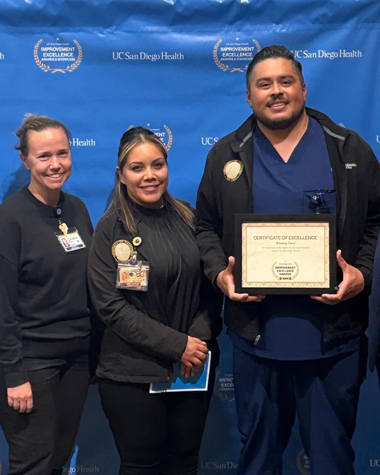 Three staff members standing in a row. Left to Right: Kelly Kemp, Ivett Ocampo and David Reyes. David is holding certificate in a frame reading “Certificate of Excellence.”