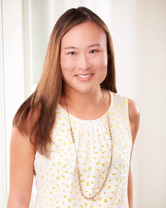 Dr. Lanna Kwon of Tryon Medical Partners smiles wearing a light sleeveless shirt in a professional portrait in front of a paned glass window