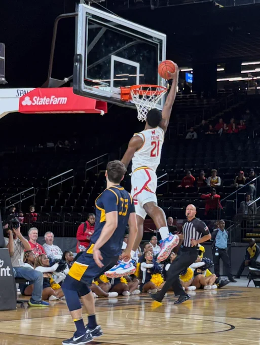 Player number 21 from Maryland scores a basketball dunk while a player from Loyola wearing jersey number 33, watches during a game.