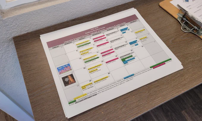Printed monthly calendar with highlighted events and notes laid on a wooden counter near a clipboard with papers inside the Resiliency & Justice Center