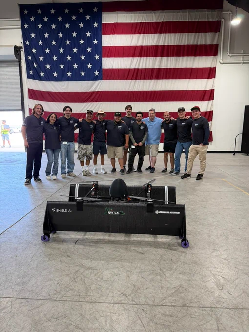 A group of people standing in front of a large American flag inside a building.