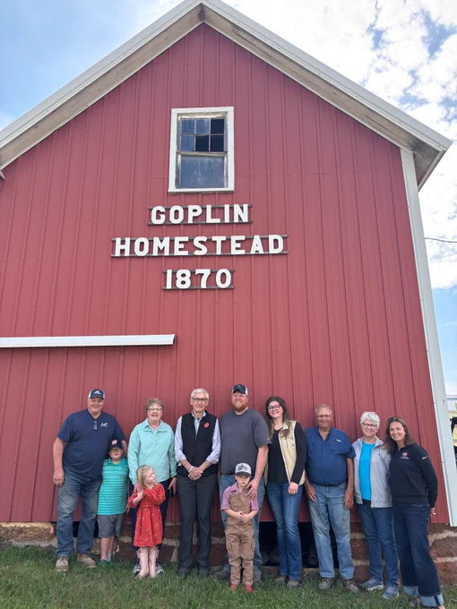 Gov. Evers poses for a photo with the Goplin family in front of barn and sign that reads "Goplin Homestead 1970"