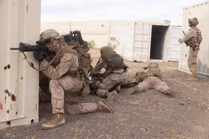 Marines establish security positions around a shipping container complex during a tactical recovery training scenario.