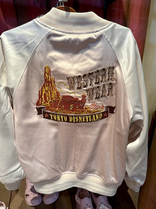 The back of a pink and white satin bomber style jacket with spiraling buttes and Big Thunder Mountain Railroad with "Western Wear" and "Tokyo Disneyland" embroidered on the back.