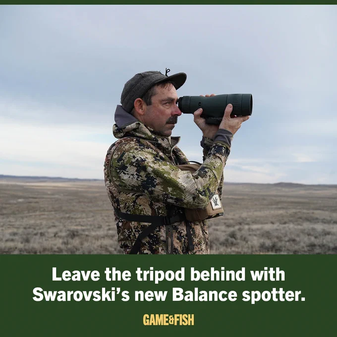 A person outdoors is using a large black Swarovski spotting scope to observe a distant landscape. They are wearing camouflage clothing and a cap. The background features open terrain under a cloudy sky. The text reads, "Leave the tripod behind with Swarovski's new Balance spotter." The image is from Game & Fish.