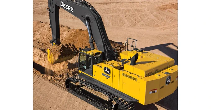 A yellow John Deere excavator is actively digging into a mound of dirt at a construction site, surrounded by a sandy landscape.