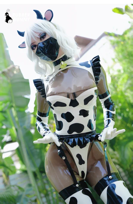 Rubberbunny奶牛纹乳胶衣户外实拍，七件独立可拆卸组件组成第二层肌肤体系，模特搭配透明黑胶打底展示奶牛斑纹设计，绿植背景突出野性美学
