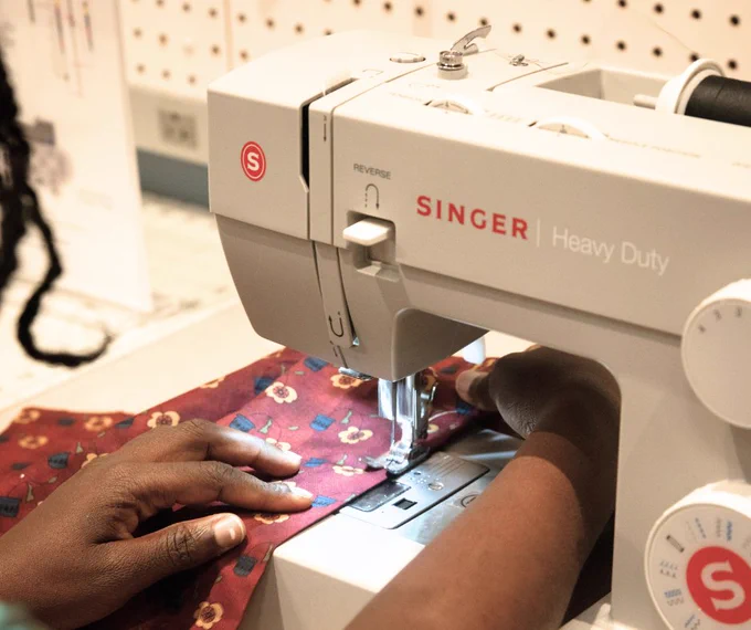 A person using a Singer Heavy Duty sewing machine, guiding red patterned fabric under the needle.