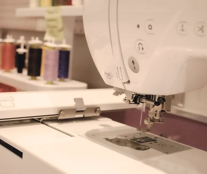 A Brother sewing machine is prominently displayed, with various colored spools of thread on a shelf in the background.