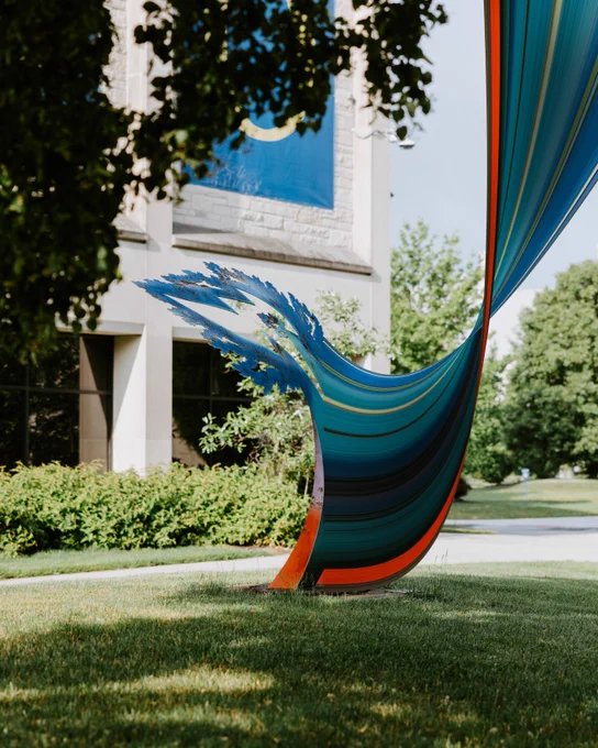 A vibrant, abstract outdoor sculpture with blue and red swirling patterns stands on Centennial Mall near the Student Union