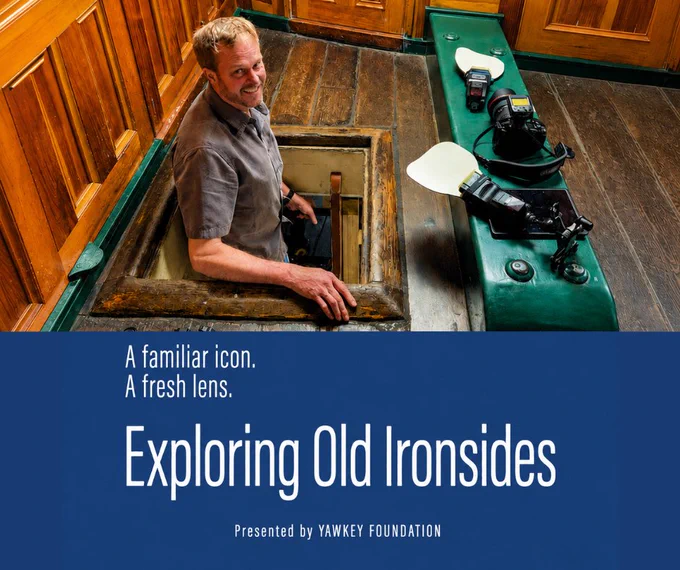Photographer emerges from below deck on a frigate, with photo equipment surrounding him. 