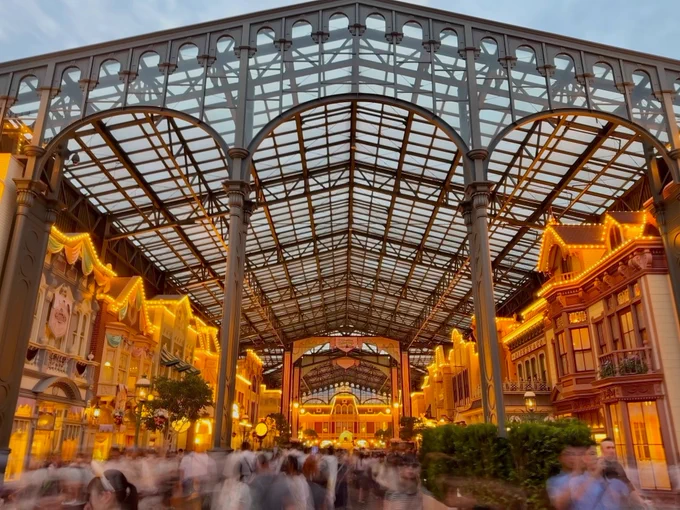 Tokyo Disneyland's World Bazaar in the early evening. "Popcorn lights" are on and outline the rooftops of the buildings. A large metal and glass structure covers the entire street.

[Eric Chu - May 27, 2026] 
