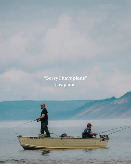 Two people fishing from a small boat on calm water with distant bluffs in the background and overlay text reading Sorry I have plans. The plans.