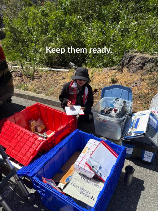 A person seated on the ground is sorting items in a red and blue plastic bin, surrounded by various containers and boxes. The text "Keep them ready." is visible at the top of the image.