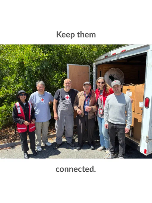A group of six people stand in front of an open Red Cross trailer filled with boxes. They are smiling, wearing various Red Cross attire, and are outdoors with greenery in the background. The text above reads "Keep them" and below reads "connected."