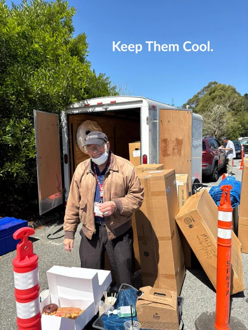A person wearing a mask stands near a trailer filled with boxes. In front of them is an open box with pastries. Traffic cones are positioned nearby. The text "Keep Them Cool" is visible at the top of the image.