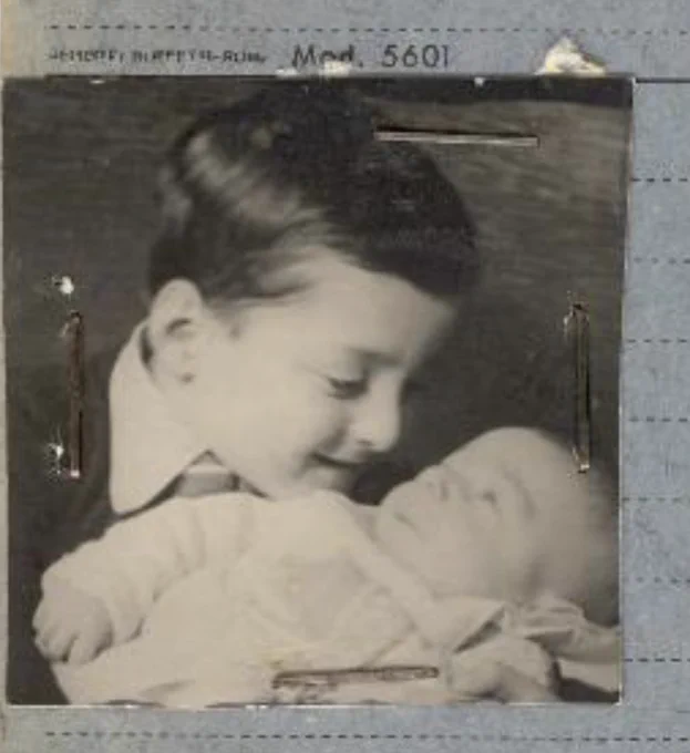Black-and-white photo of a smiling boy holding a baby. 