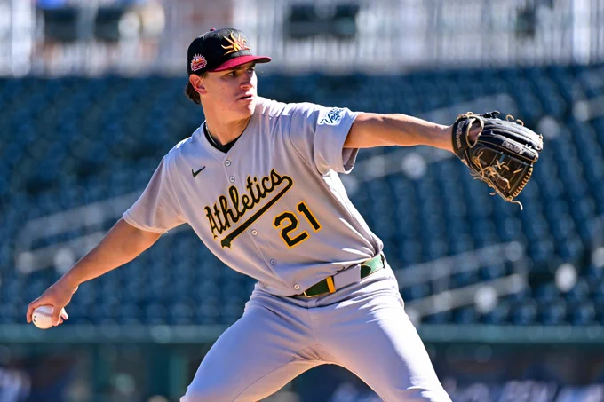 Nathan Dettmer winds up to throw a pitch while wearing a gray uniform with "Athletics" and the number 21 on the front.