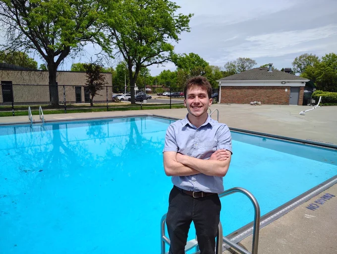 Jacob Ames Pool Manager with his arms crossed standing on the pool deck at the  Parma Heights Pool by a ladder and pool is full of water. 