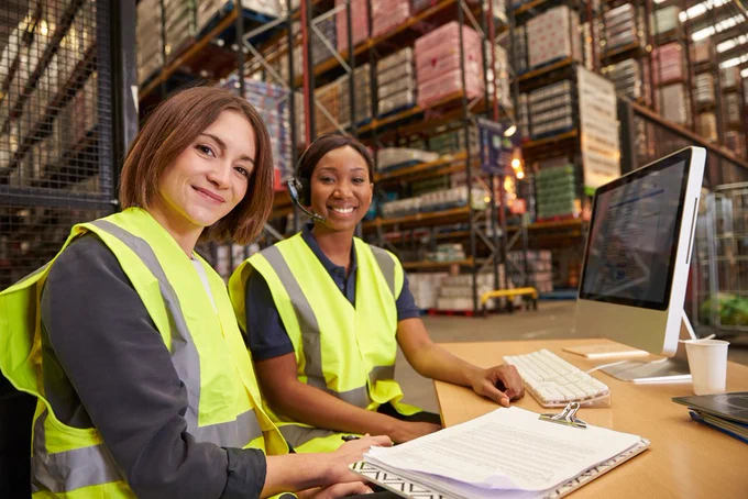 Two women sat at a desk working in a warehouse