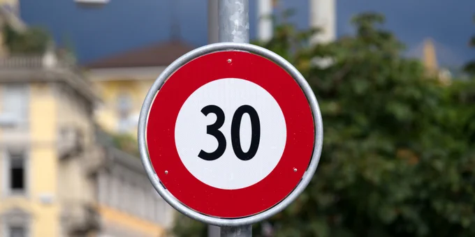 Ein rundes, rotes Verkehrsschild mit Tempo 30 ist an einem Metallmast befestigt.