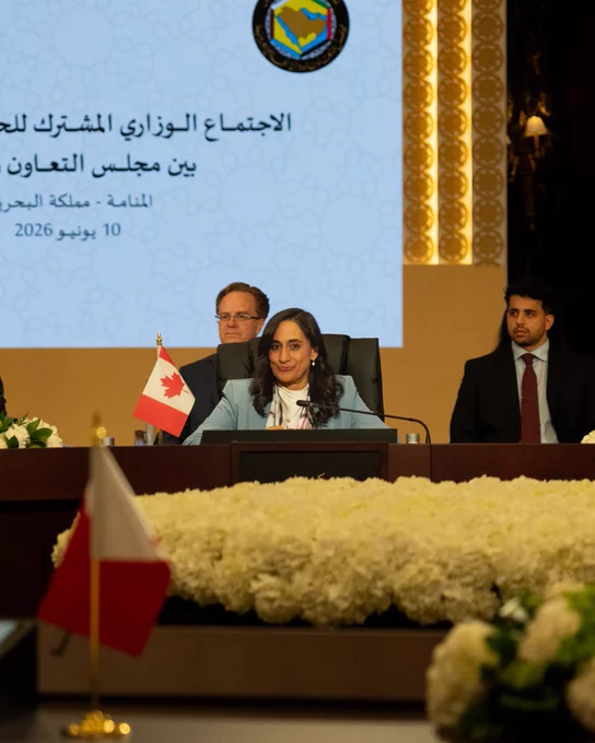 Minister Anand seated at a table during a Gulf Cooperation Council meeting, with a Canadian flag and a conference backdrop in the background.