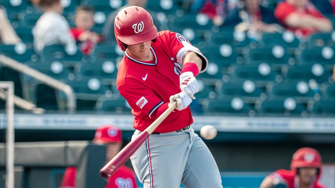 Eli Willits swings the bat wearing a red Washington Nationals jersey, helmet and gray pants