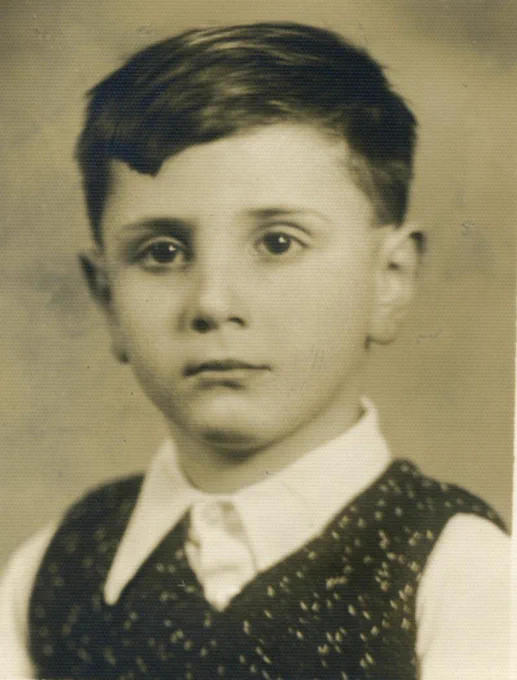 Vintage black and white photo of a young boy with short hair wearing a vest and shirt, staring directly at the camera.
