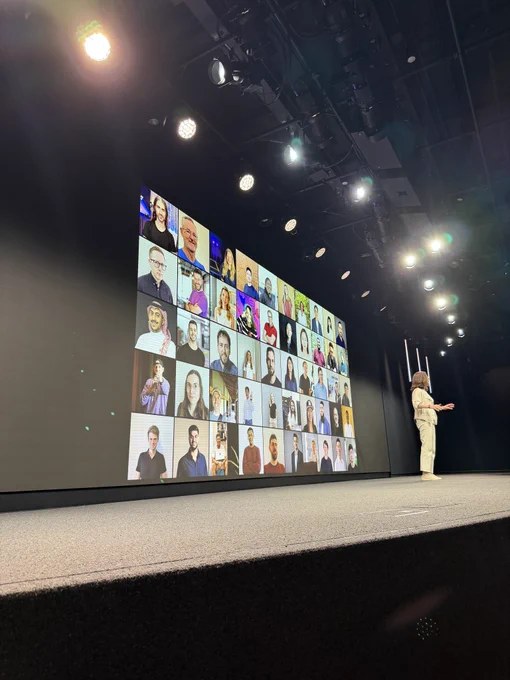 Photo of Susan Prescott on stage in front of the display showing the grid of community leaders, with Aled’s face in the top left area.