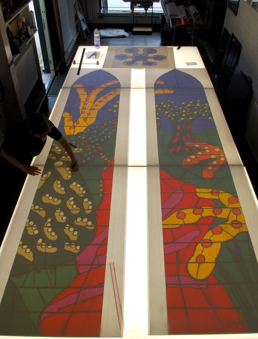 A design for a colouful stained glass window laid out on a large lightbox in an artist's studio
