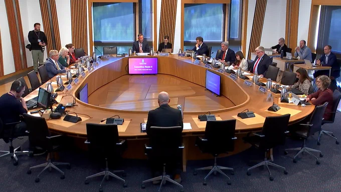 A Committe room in the Scottish Parliament, with MSPs sitting around a large oval committee table